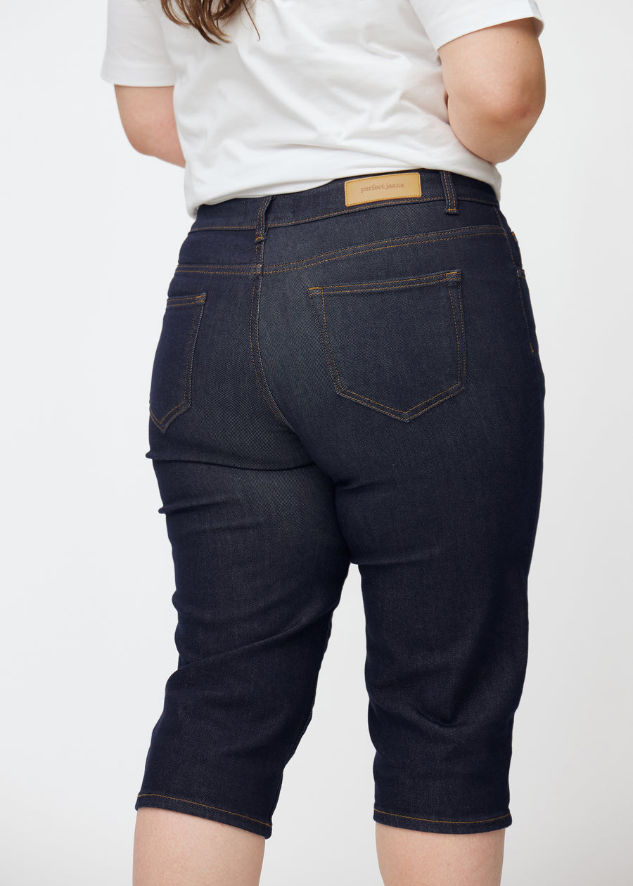 Dyp mørkeblå denim capris til dame i fargen Midnights sett bakfra i nærbilde på plus-size modell.