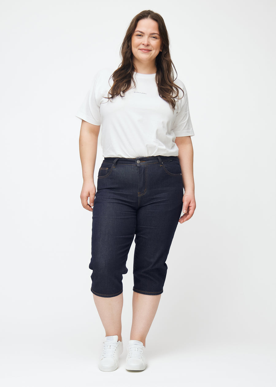 Helbilde av plus-size modell i dyp mørkeblå denim capris til dame i fargen Midnights med slim passform.