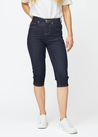 Dyp mørkeblå denim capris til dame i fargen Midnights med slim passform som er figursydd fra hoften til under kneet, sett forfra.