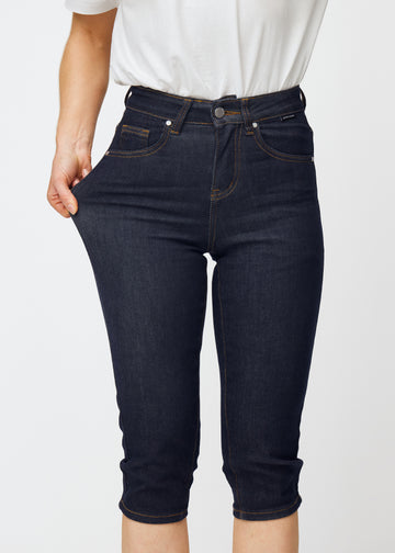 Modell strekker dyp mørkeblå denim capris til dame i fargen Midnights ved låret for å vise materialets stretch.