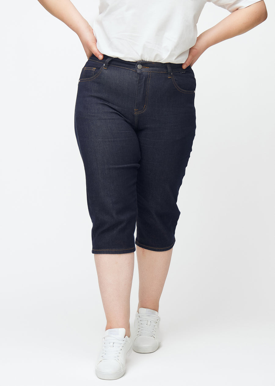 Dyp mørkeblå denim capris til dame i fargen Midnights med slim passform sett forfra på plus-size modell.