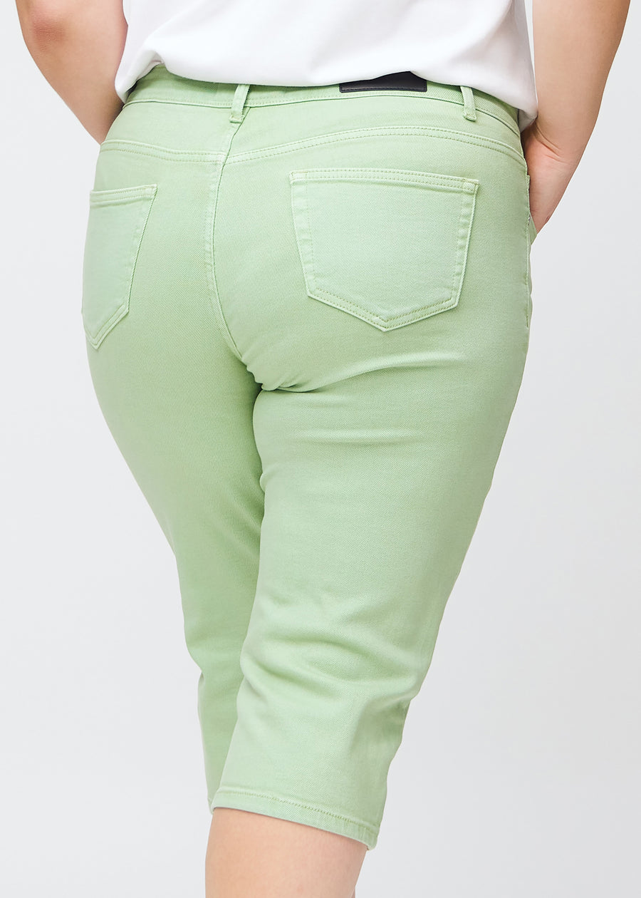 Slim-capris til kvinner i pastelllysegrønt jeansstoff, fargen Mints. Nærbilde bakfra på en plus size-modell, med fokus på baklommer og sømmer.