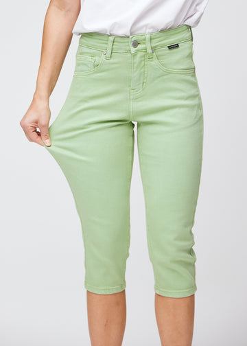 Slim-capris til kvinner i pastelllysegrønt jeansstoff, fargen Mints. En modell strekker stoffet ved låret for å vise stretch og fleksibilitet.