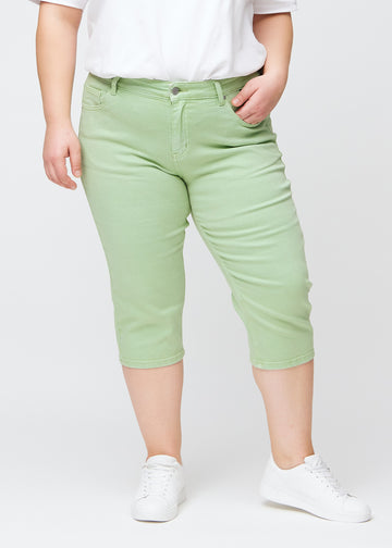 Slim-capris til kvinner i pastelllysegrønt jeansstoff, fargen Mints. Sett forfra på en plus size-modell, med figursydd passform til rett under kneet.