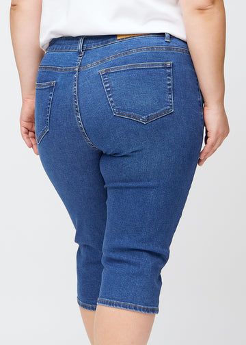 Slim-capris til kvinner i mørkeblå denim, fargen Oceans. Nærbilde bakfra på en plus size-modell, med fokus på baklommer og sømmer.