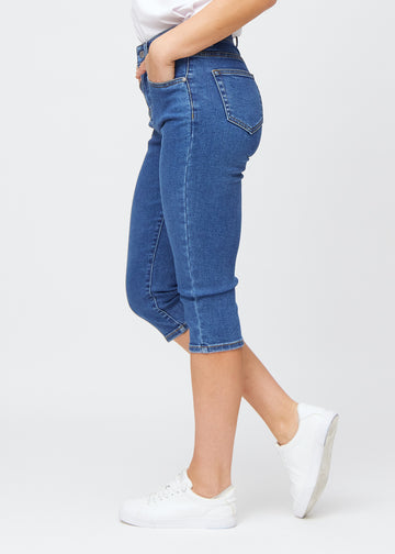 Slim-capris til kvinner i mørkeblå denim, fargen Oceans. Sett fra siden på en modell, med figursydd passform og mellomhøyt liv (Mid Rise).