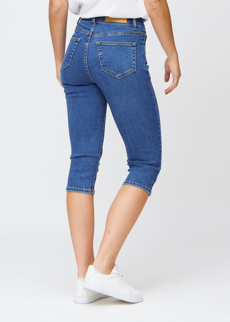 Slim-capris til kvinner i mørkeblå denim, fargen Oceans. Sett bakfra på en modell, med fokus på passform, lengde og baklommer.