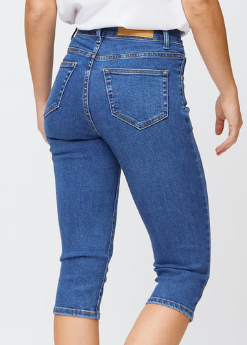 Slim-capris til kvinner i mørkeblå denim, fargen Oceans. Nærbilde bakfra på en modell, med fokus på baklommer og sømmer.