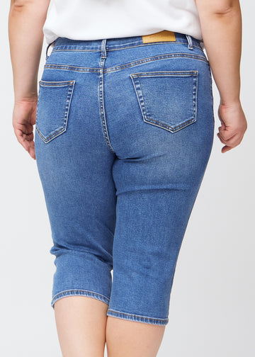Slim-capris til kvinner i blå denim, fargen Rivers. Nærbilde bakfra på en plus size-modell, med fokus på baklommer og sømmer.