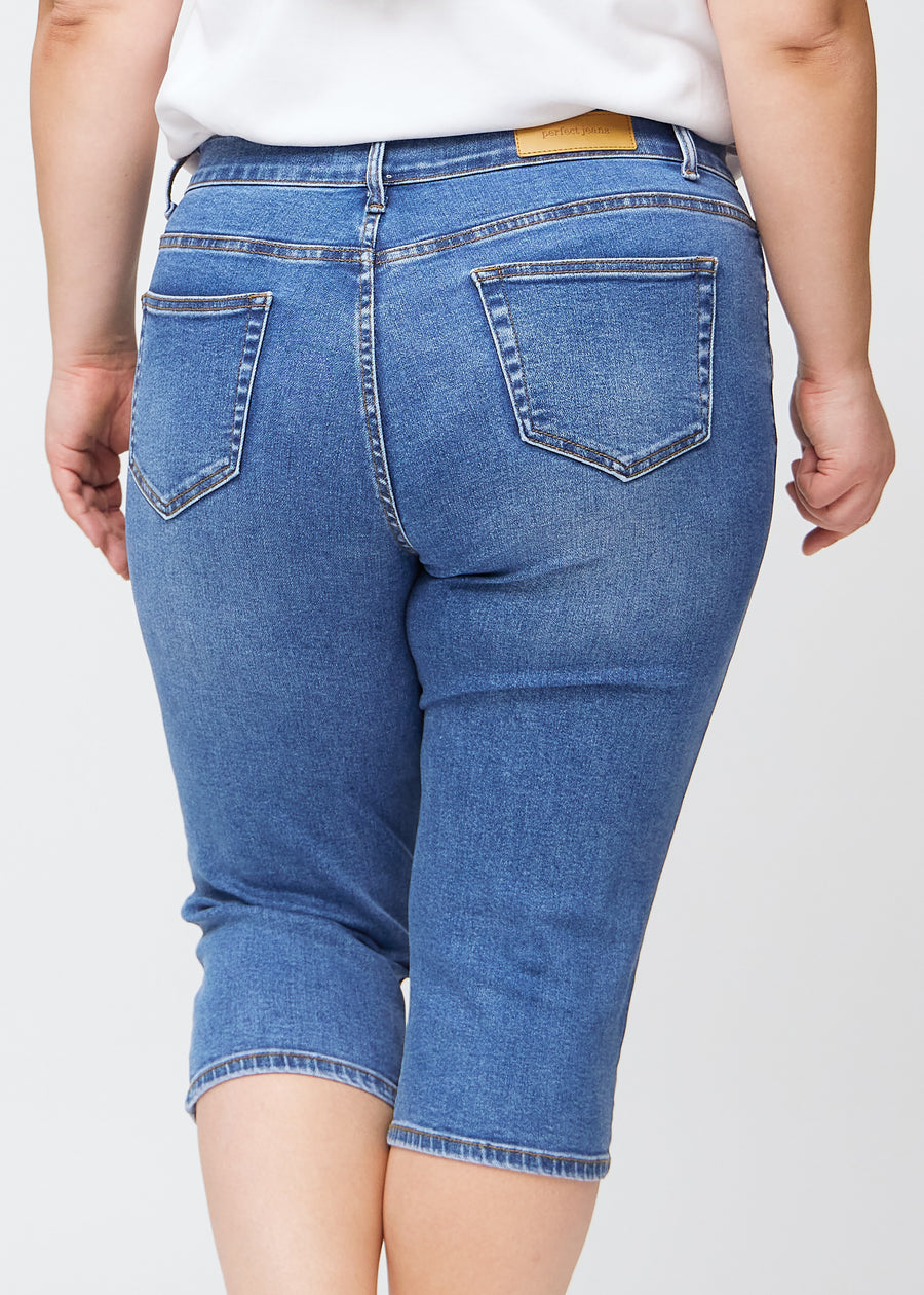Slim-capris til kvinner i blå denim, fargen Rivers. Nærbilde bakfra på en plus size-modell, med fokus på baklommer og sømmer.