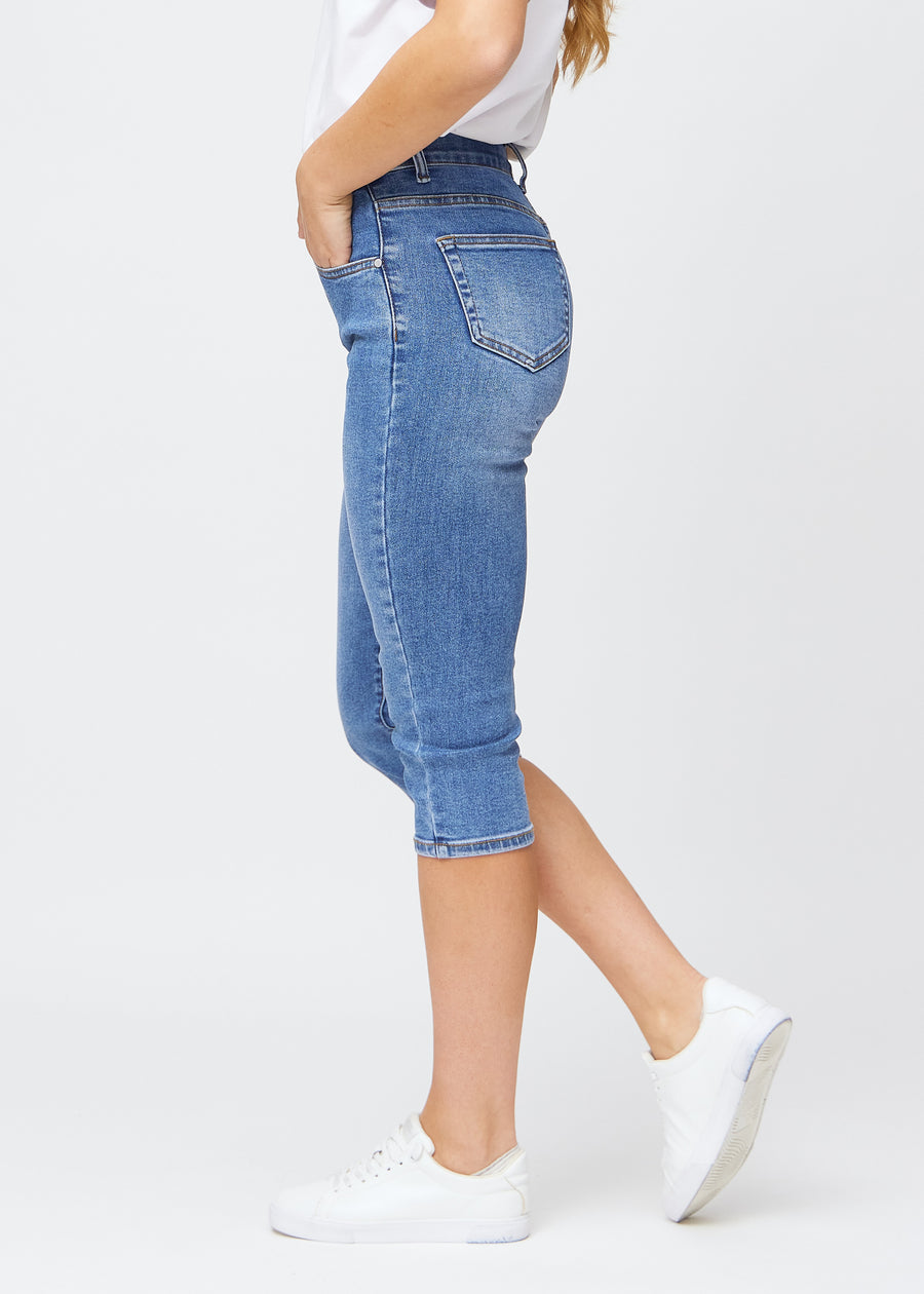 Slim-capris til kvinner i blå denim, fargen Rivers. Sett fra siden på en modell, med figursydd passform og mellomhøyt liv (Mid Rise).