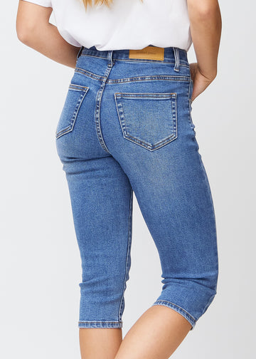 Slim-capris til kvinner i blå denim, fargen Rivers. Nærbilde bakfra på en modell, med fokus på baklommer og sømmer.