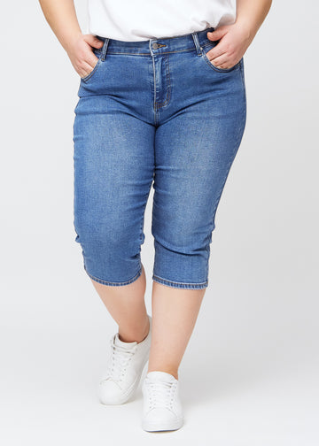 Slim-capris til kvinner i blå denim, fargen Rivers. Sett forfra på en plus size-modell, med figursydd passform til rett under kneet.