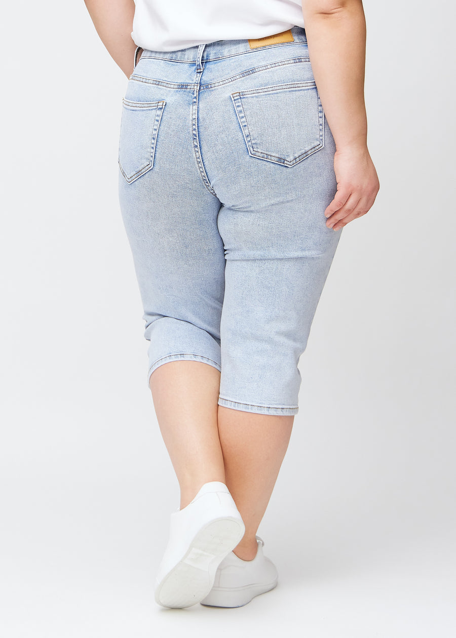 Slim-capris til kvinner i lyseblå denim, fargen Waves. Sett bakfra på en plus size-modell, med fokus på passform, lengde og baklommer.