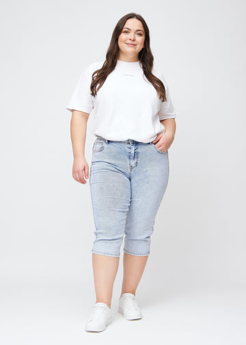 Slim-capris til kvinner i lyseblå denim, fargen Waves. Helhetsbilde av en plus size-modell med slim-capris.