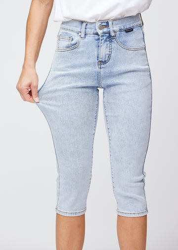 Slim-capris til kvinner i lyseblå denim, fargen Waves. En modell strekker stoffet ved låret for å vise stretch og fleksibilitet.