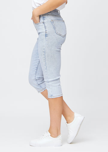 Slim-capris til kvinner i lyseblå denim, fargen Waves. Sett fra siden på en modell, med figursydd passform og mellomhøyt liv (Mid Rise).