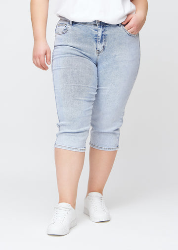 Slim-capris til kvinner i lyseblå denim, fargen Waves. Sett forfra på en plus size-modell, med figursydd passform til rett under kneet.