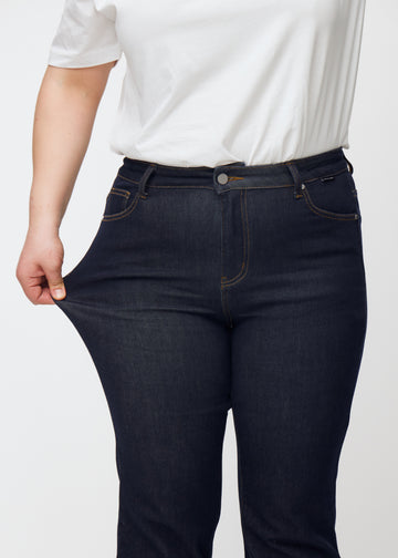 Plus-size-modell strekker dyp mørkeblå denim jeans til kvinner i fargen Midnights ved låret for å vise materialets stretch.