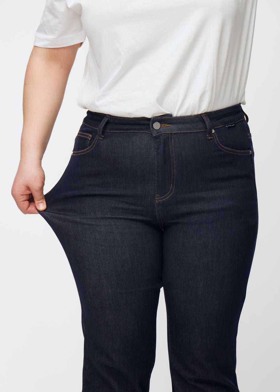 Plus-size-modell strekker dyp mørkeblå denim jeans til kvinner i fargen Midnights ved låret for å vise materialets stretch.