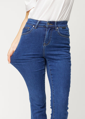 Mørkeblå mid-rise bootcut-jeans i fargen Oceans. En modell strekker jeansstoffet ved låret for å vise stretchen.