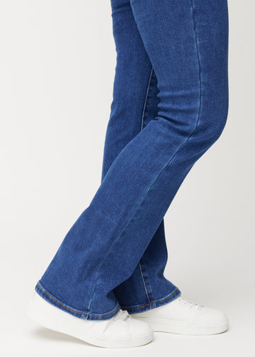 Mørkeblå mid-rise bootcut-jeans i fargen Oceans. Nærbilde ved ankelen på en modell som viser den lette utsvingen nederst.