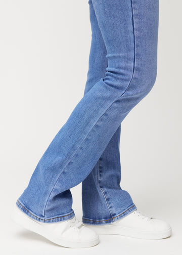 Blå mid-rise bootcut-jeans i fargen Rivers. Nærbilde ved ankelen på en modell som viser den lette utsvingen nederst.