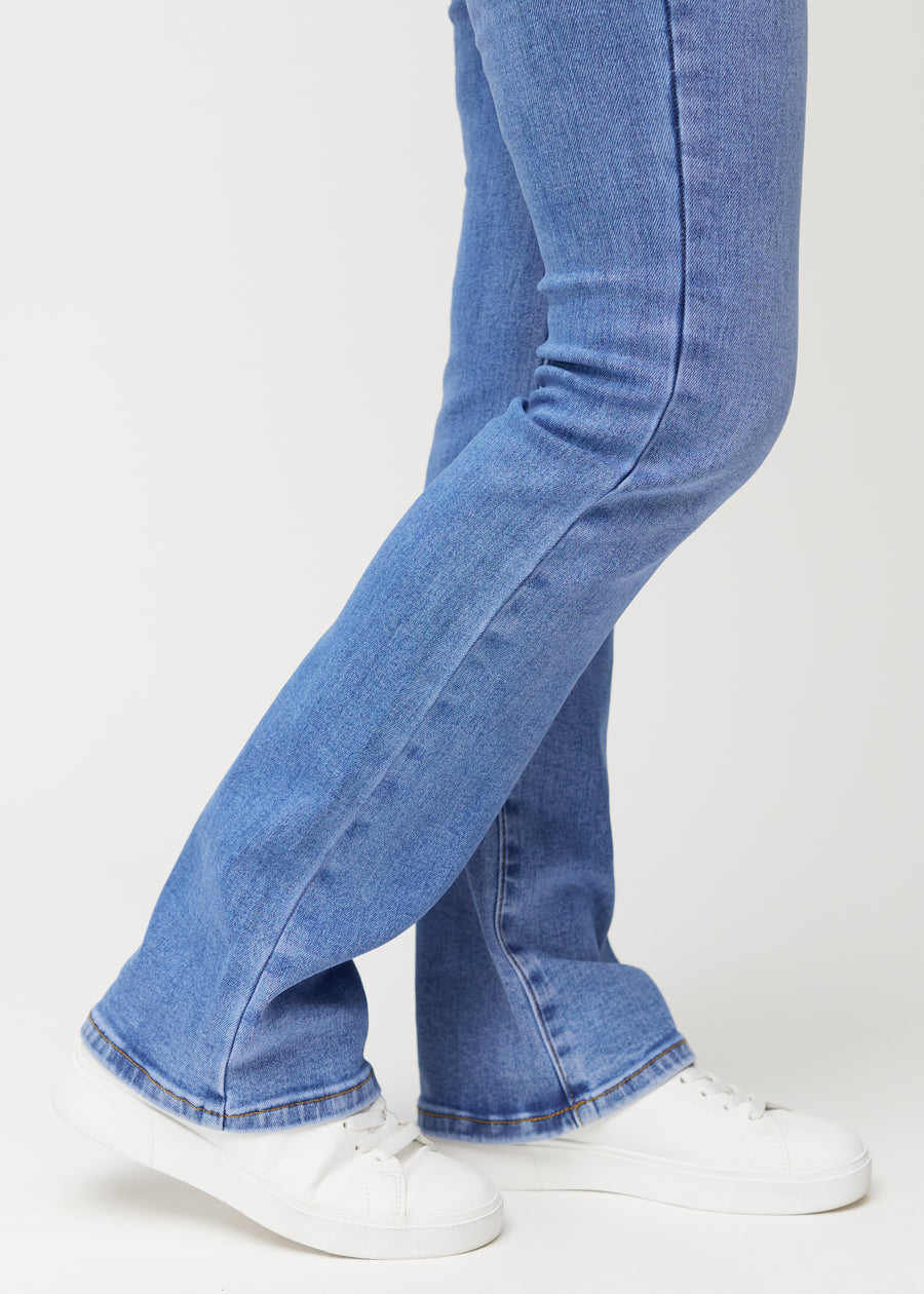 Blå mid-rise bootcut-jeans i fargen Rivers. Nærbilde ved ankelen på en modell som viser den lette utsvingen nederst.