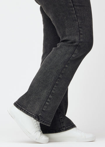 Mørkegrå mid-rise bootcut-jeans i fargen Shadows. Nærbilde ved ankelen på en plus size-modell som viser den lette utsvingen nederst.