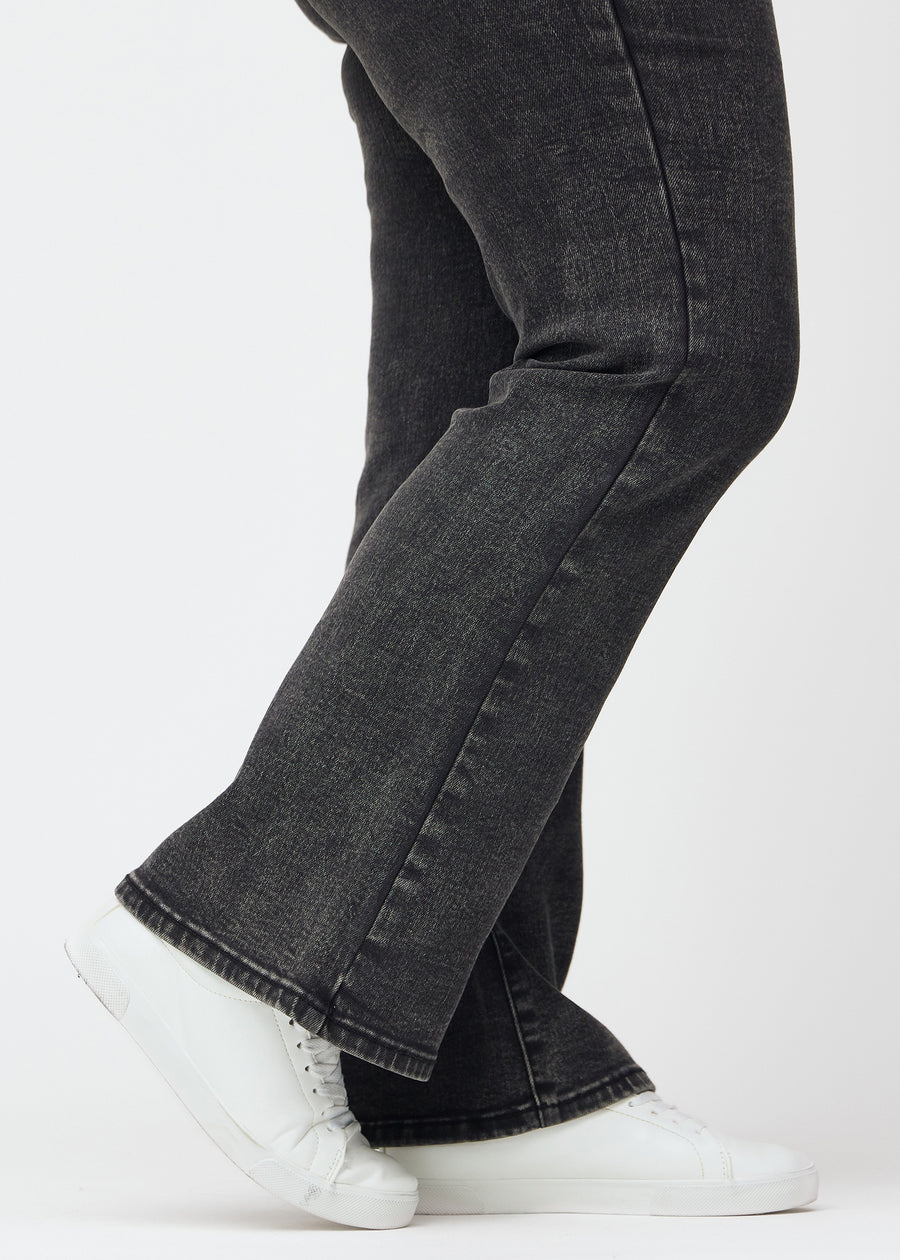 Mørkegrå mid-rise bootcut-jeans i fargen Shadows. Nærbilde ved ankelen på en plus size-modell som viser den lette utsvingen nederst.