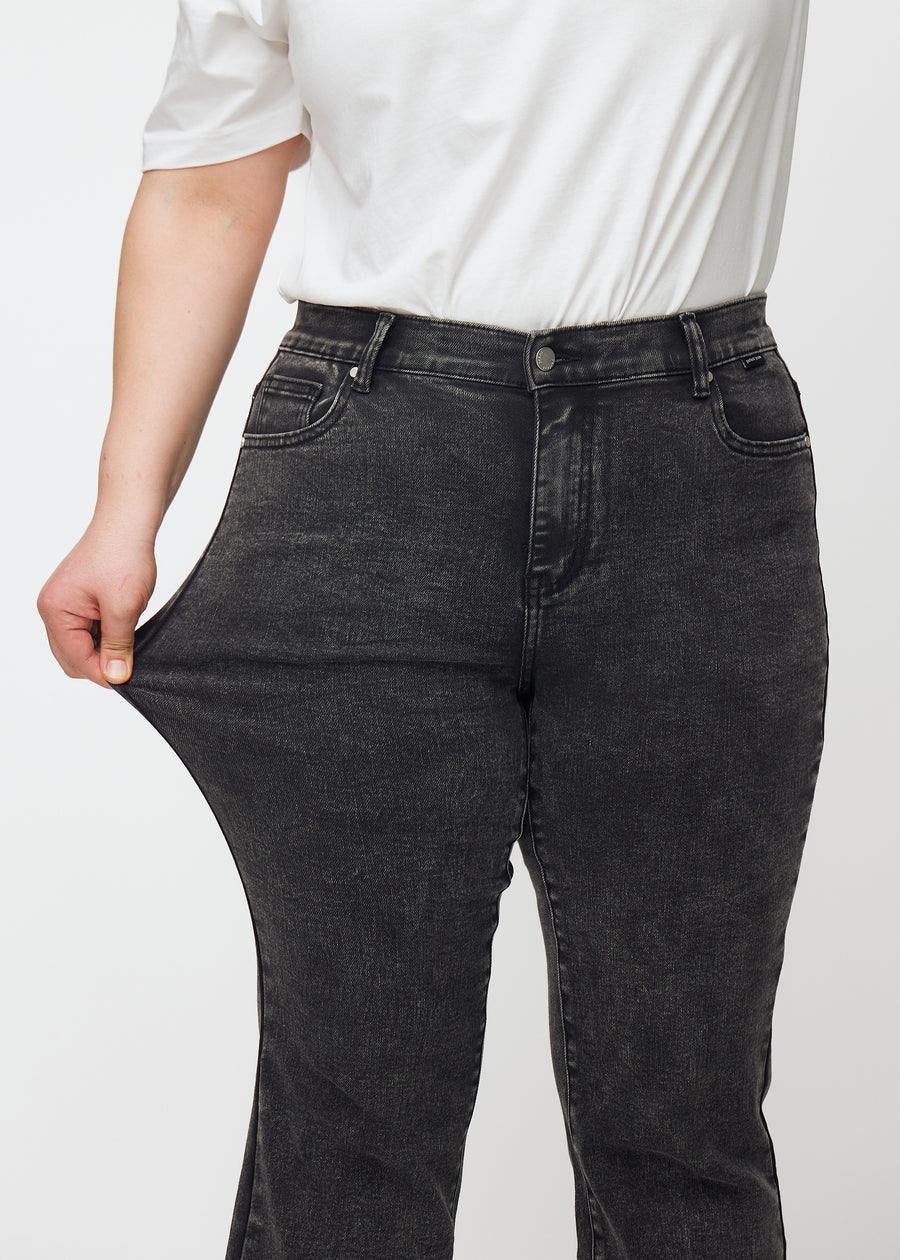 Mørkegrå mid-rise bootcut-jeans i fargen Shadows. En plus size-modell strekker jeansstoffet ved låret for å vise stretchen.