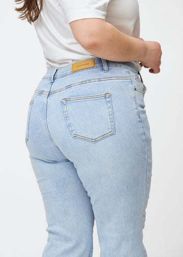 Lyseblå mid-rise bootcut-jeans i fargen Waves. Nærbilde bakfra på en plus size-modell for å vise detaljene.