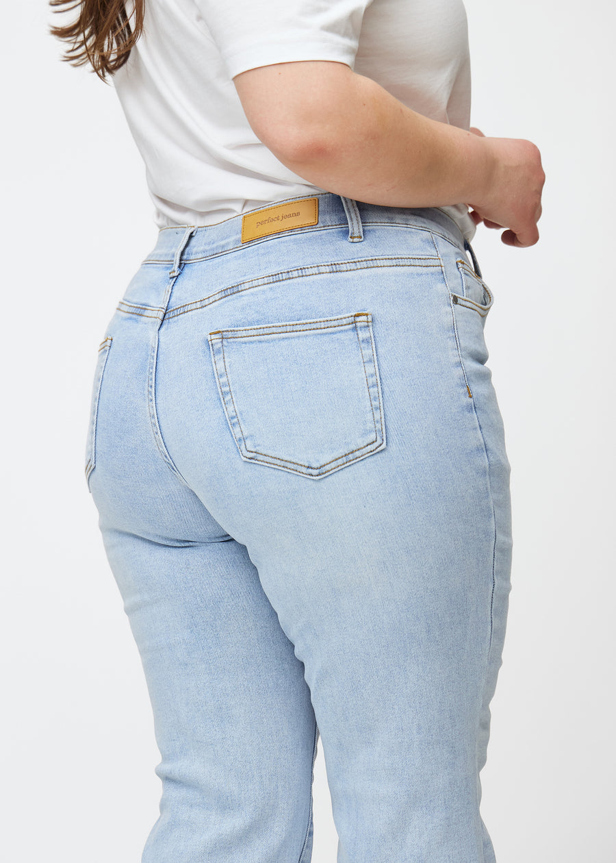 Lyseblå mid-rise bootcut-jeans i fargen Waves. Nærbilde bakfra på en plus size-modell for å vise detaljene.