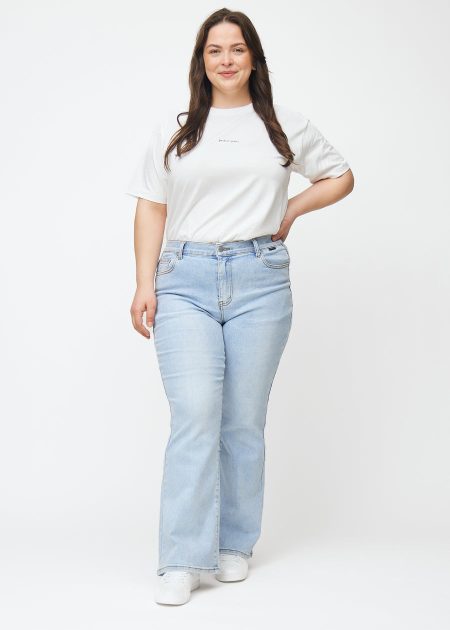 Lyseblå mid-rise bootcut-jeans i fargen Waves. Helhetsbilde av en plus size-modell med jeansene på.