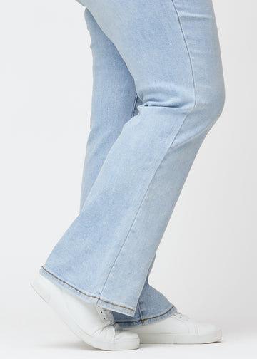 Lyseblå mid-rise bootcut-jeans i fargen Waves. Nærbilde ved ankelen på en plus size-modell som viser den lette utsvingen nederst.
