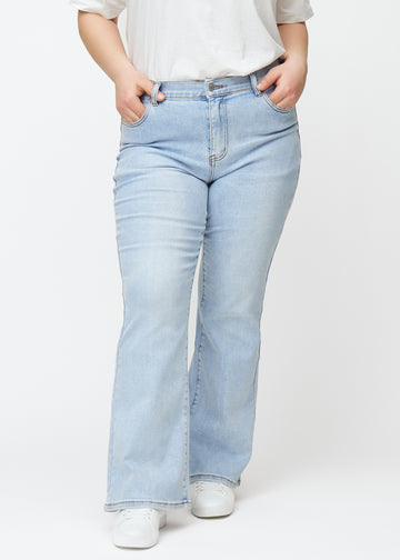 Lyseblå mid-rise bootcut-jeans i fargen Waves. Sett forfra på en plus size-modell, med tettsittende passform over hofter og lår og lett utsving nederst.