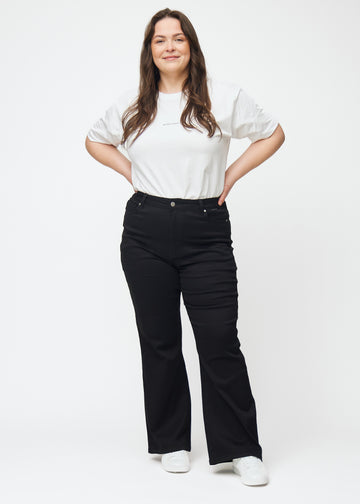 Fullt bilde av en plus-size-modell i svarte høytaljede bootcut jeans.