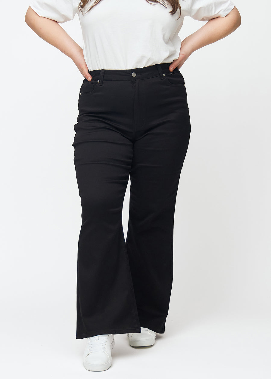 Svarte høytaljede bootcut jeans, modellnavn Ravens, som sitter tett fra midje til lår og har en lett sleng nederst, på en plus-size-modell, sett forfra.