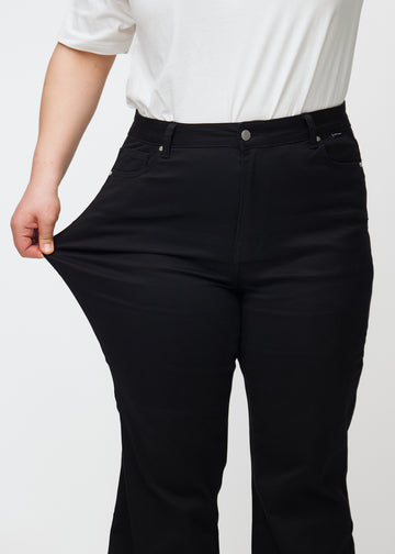 Plus-size-modellen strekker jeansene ved låret for å vise stretch.