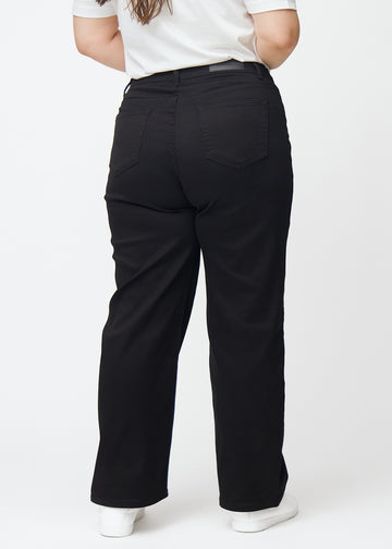 Svarte høytlivede jeans, som sitter til i midjen og har en løs passform med vidde nedover, sett bakfra på en plus-size-modell slik at man kan se hele produktet.