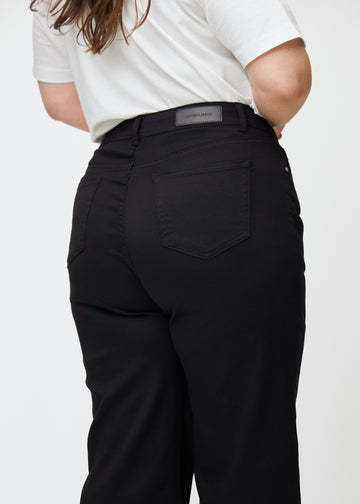 Svarte høytlivede jeans, som sitter til i midjen og har en løs passform med vidde nedover, sett tett på bakfra på en plus-size-modell for å vise detaljer.