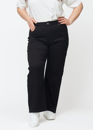 Svarte høytlivede jeans av modellen Ravens, som sitter til i midjen og har en løs passform med vidde nedover, på en plus-size-modell sett forfra.