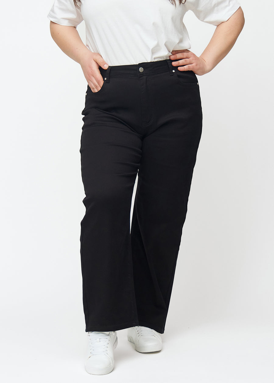 Svarte høytlivede jeans av modellen Ravens, som sitter til i midjen og har en løs passform med vidde nedover, på en plus-size-modell sett forfra.
