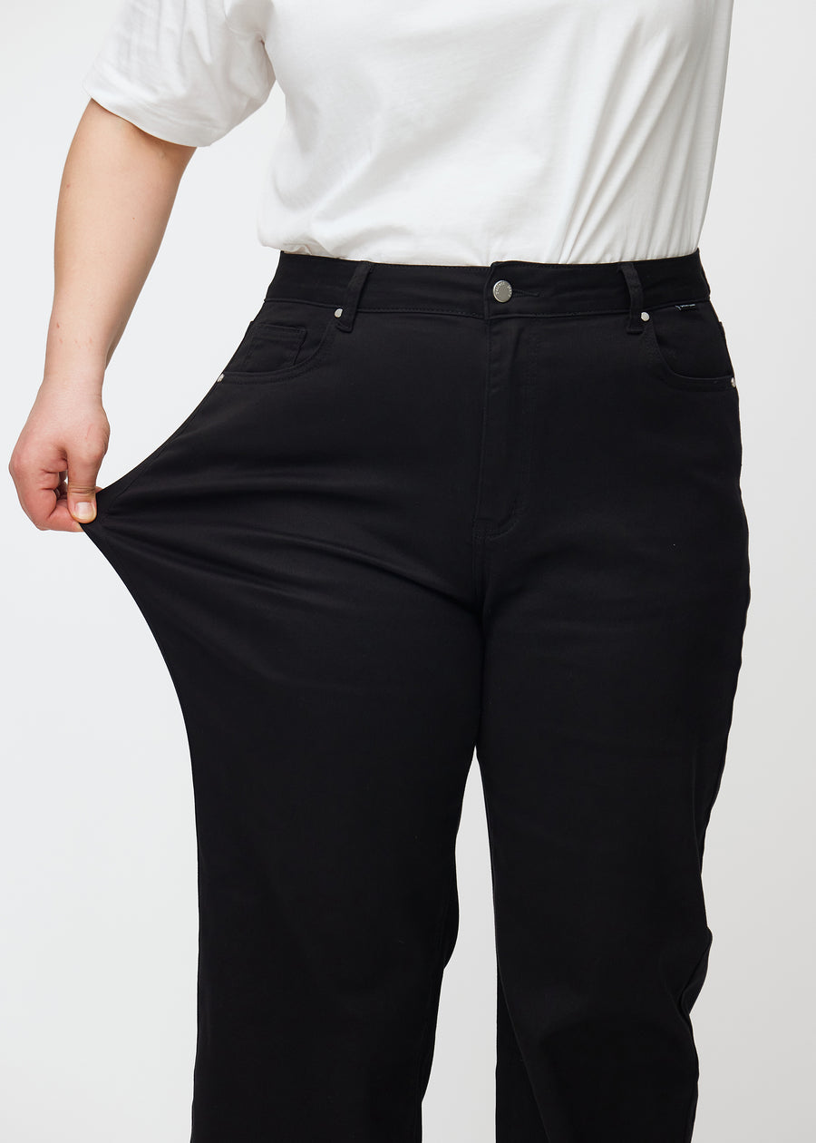 Plus-size-modellen strekker jeansene ved låret for å vise stretch.