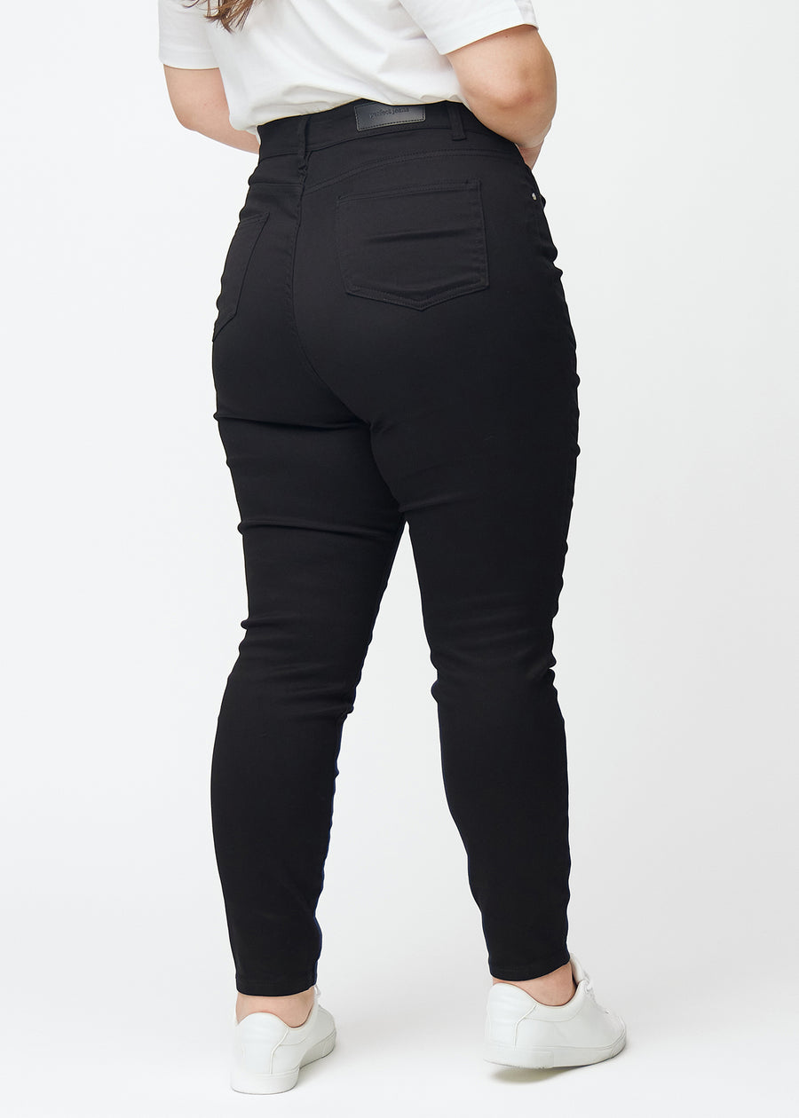 Svarte plus size jeans med høy midje i fargen Ravens med skinny fit vises bakfra på en modell.