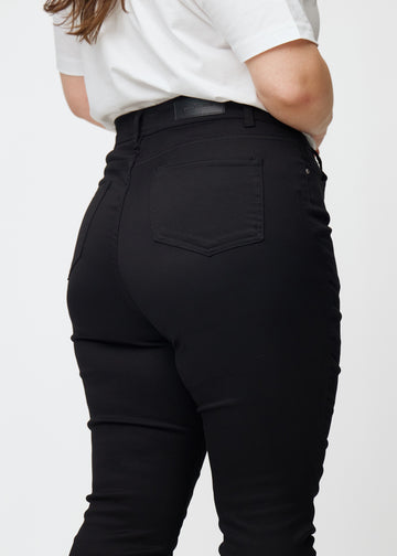 Bildet viser et nærbilde av svarte plus size high rise jeans til kvinner i fargen Ravens i skinny fit sett bakfra.