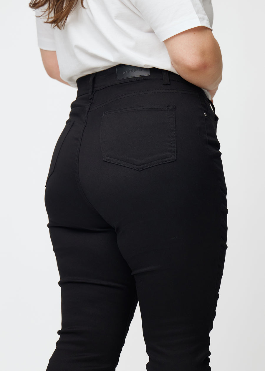 Bildet viser et nærbilde av svarte plus size high rise jeans til kvinner i fargen Ravens i skinny fit sett bakfra.