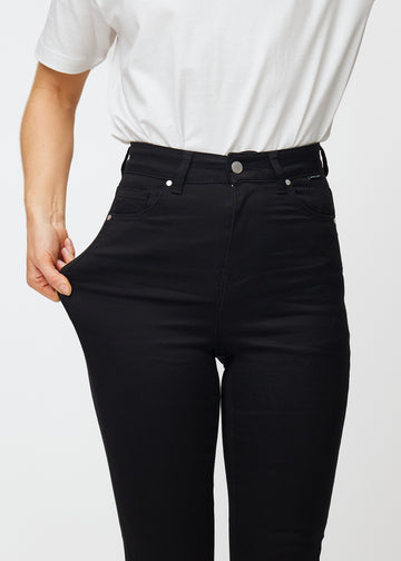 En modell strekker de svarte Ravens stretch jeans med høy midje for å illustrere passformen.
