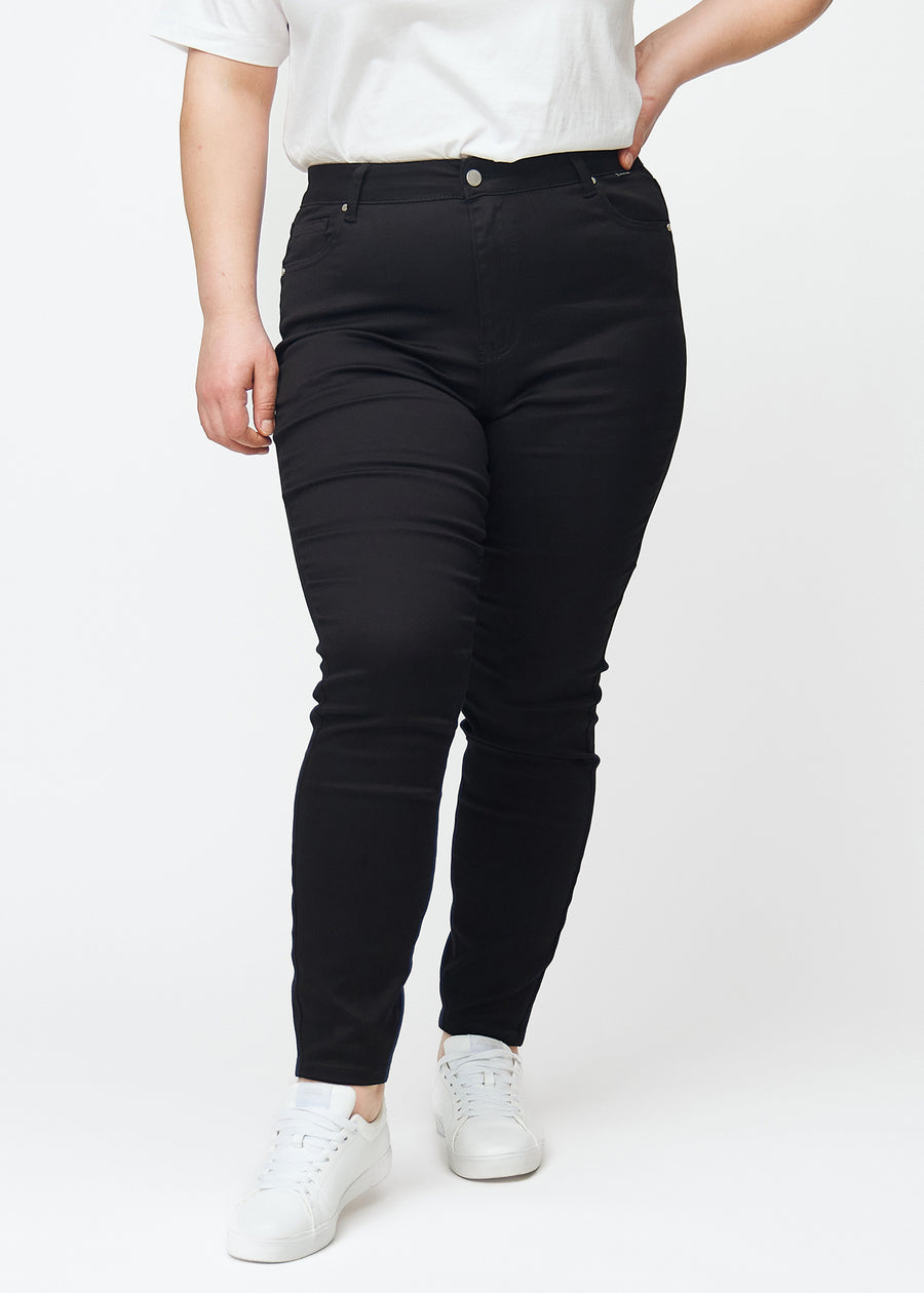 En plus size-modell viser frem svarte high rise skinny jeans til kvinner i fargen Ravens sett forfra.