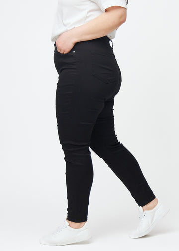Svarte plus size high rise skinny jeans til kvinner i fargen Ravens vises fra siden på en modell.